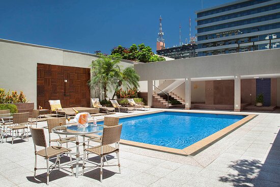 Foto da área externa de um hotel em Brasília. Na foto, uma piscina com mesas ao redor.
