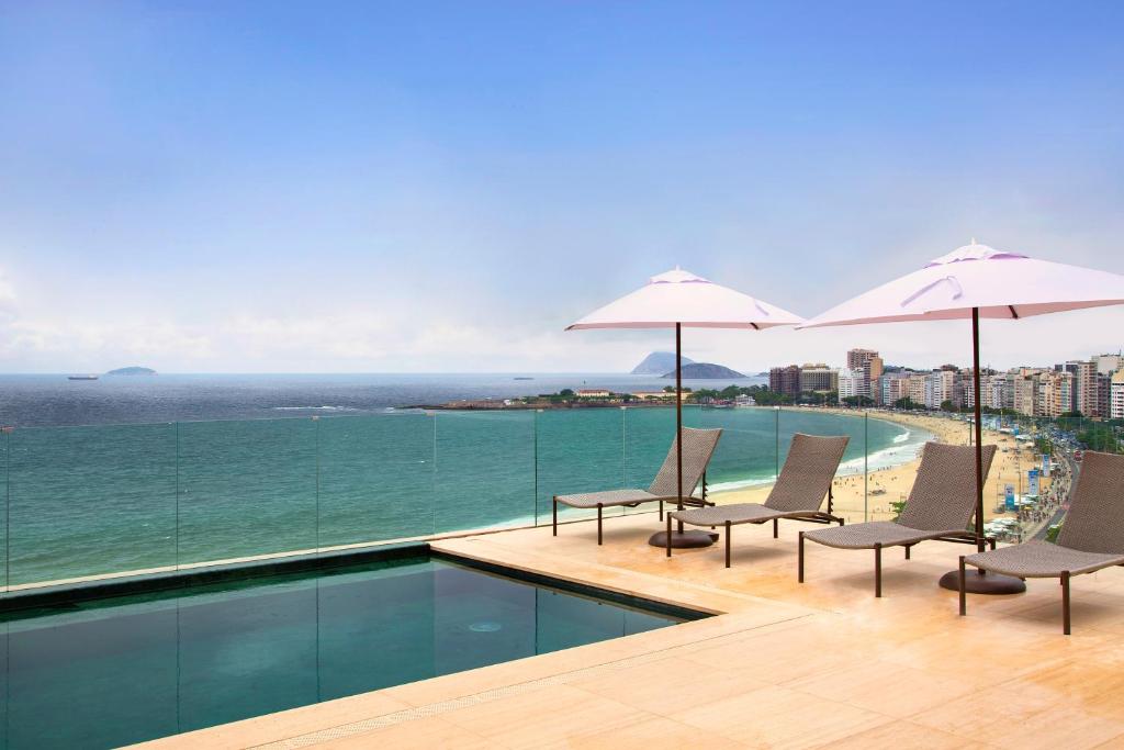 Foto da cobertura de um hotel da Rede Windsor em Copacabana. Na foto, uma piscina e uma mesa com um guarda sol, com o horizonte ao fundo.