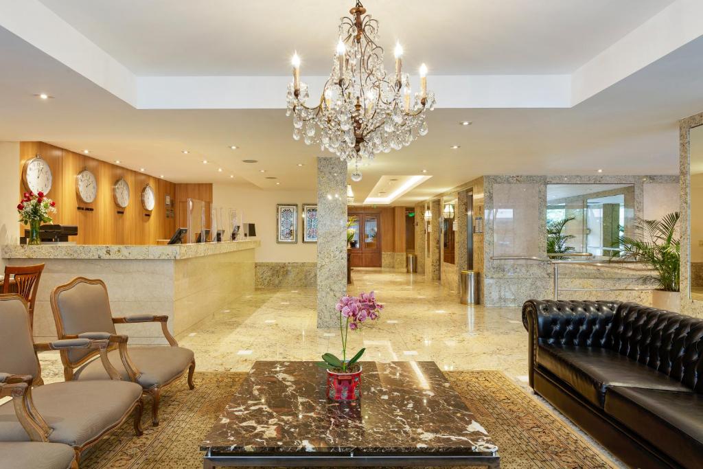 Foto da recepção de um hotel da Rede Windsor em Copacabana. Na foto, um lustre, cadeiras, sofás, espelhos e uma mesa de centro.