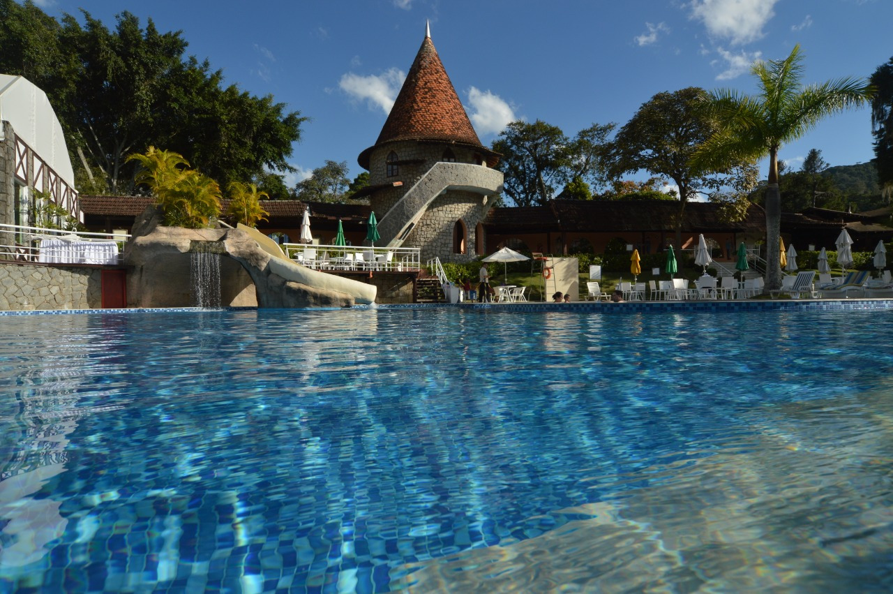 imagem de dentro da piscina do resort Le Canton Village. no fundo da imagem, há parte do castelo e cadeiras na beira da piscina