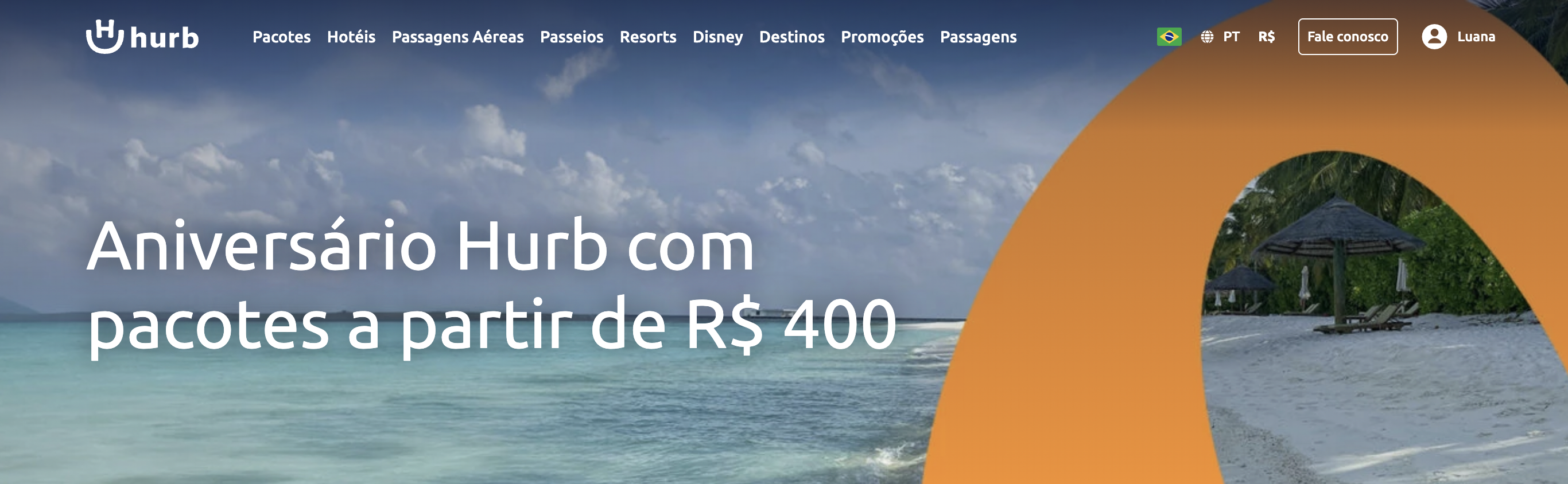 O banner do website da Hurb destaca uma promoção de aniversário com pacotes a partir de R$ 400, exibindo uma paisagem de praia tranquila e tropical com guarda-sóis de palha e águas cristalinas como plano de fundo.