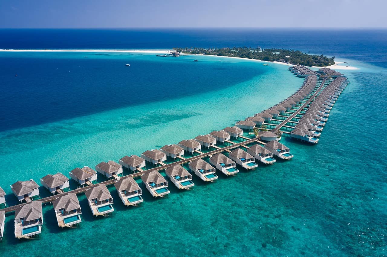 Vista aérea deslumbrante de bangalôs de luxo em fileira, estendendo-se sobre o tranquilo mar turquesa das Maldivas, exemplificando o refúgio tropical perfeito para viajantes. desconto-pix