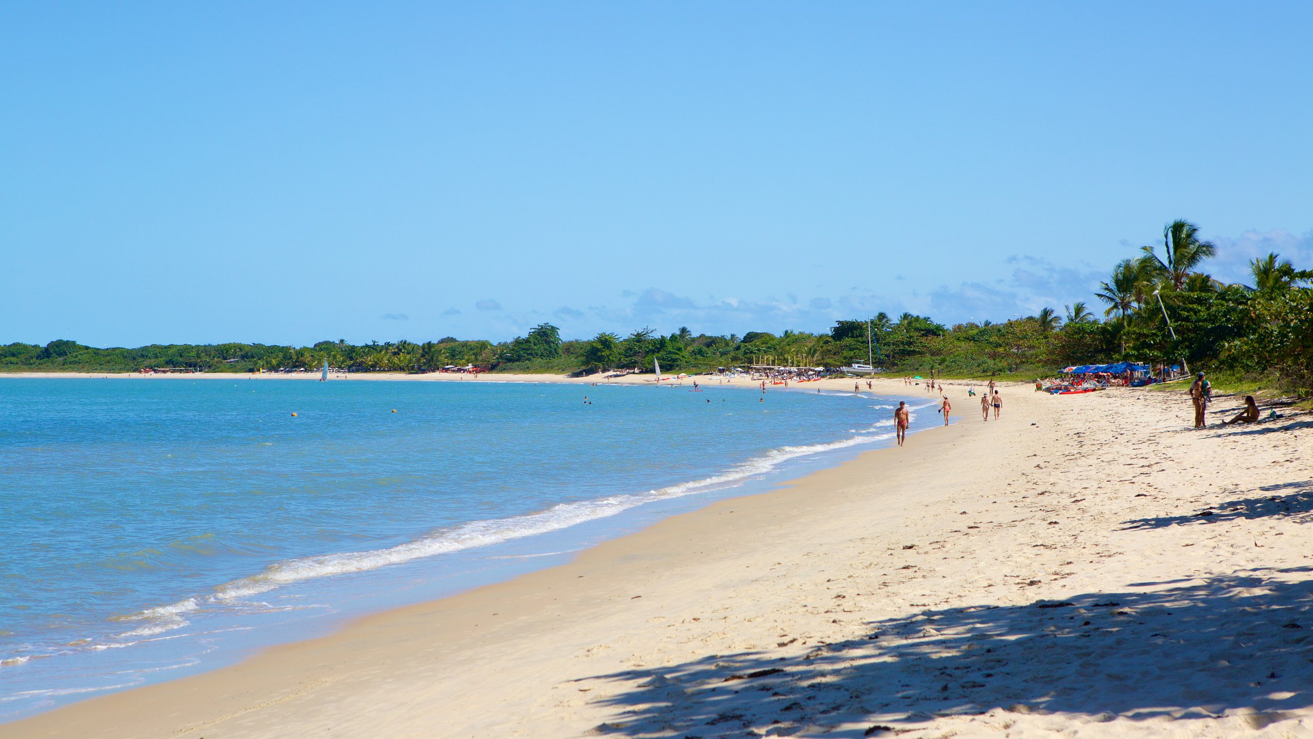 Vista ensolarada da Praia do Mutá em Porto Seguro, com areia branca, águas calmas e pessoas desfrutando do ambiente relaxante.