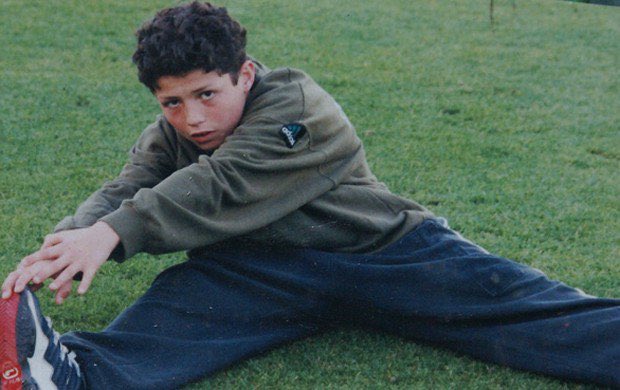 Menino jovem fazendo alongamento em um campo de futebol.