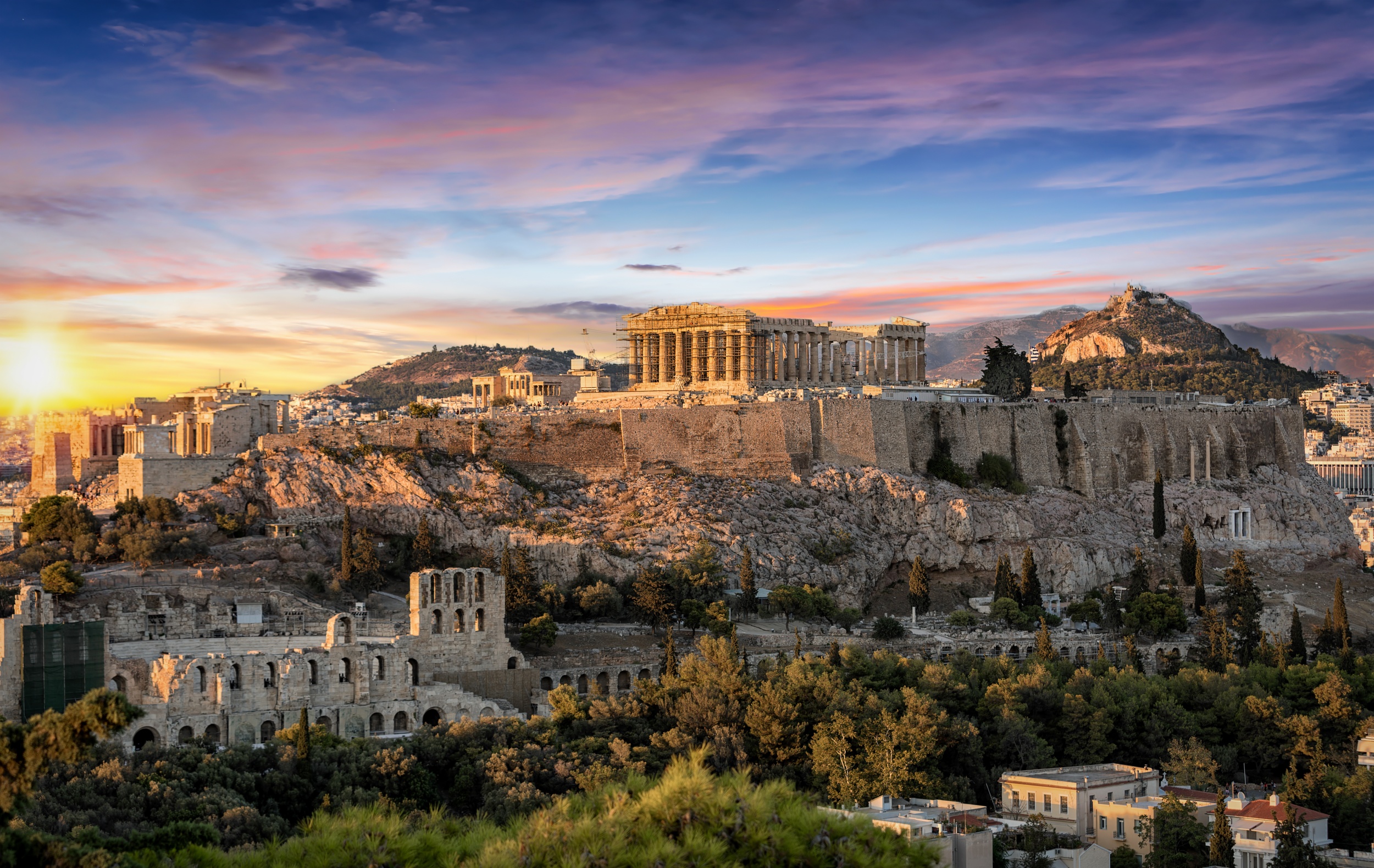 Vista do Parthenon e do Odeão de Herodes Ático na Acrópole de Atenas, capturada ao pôr do sol, com o Monte Licabeto ao fundo.