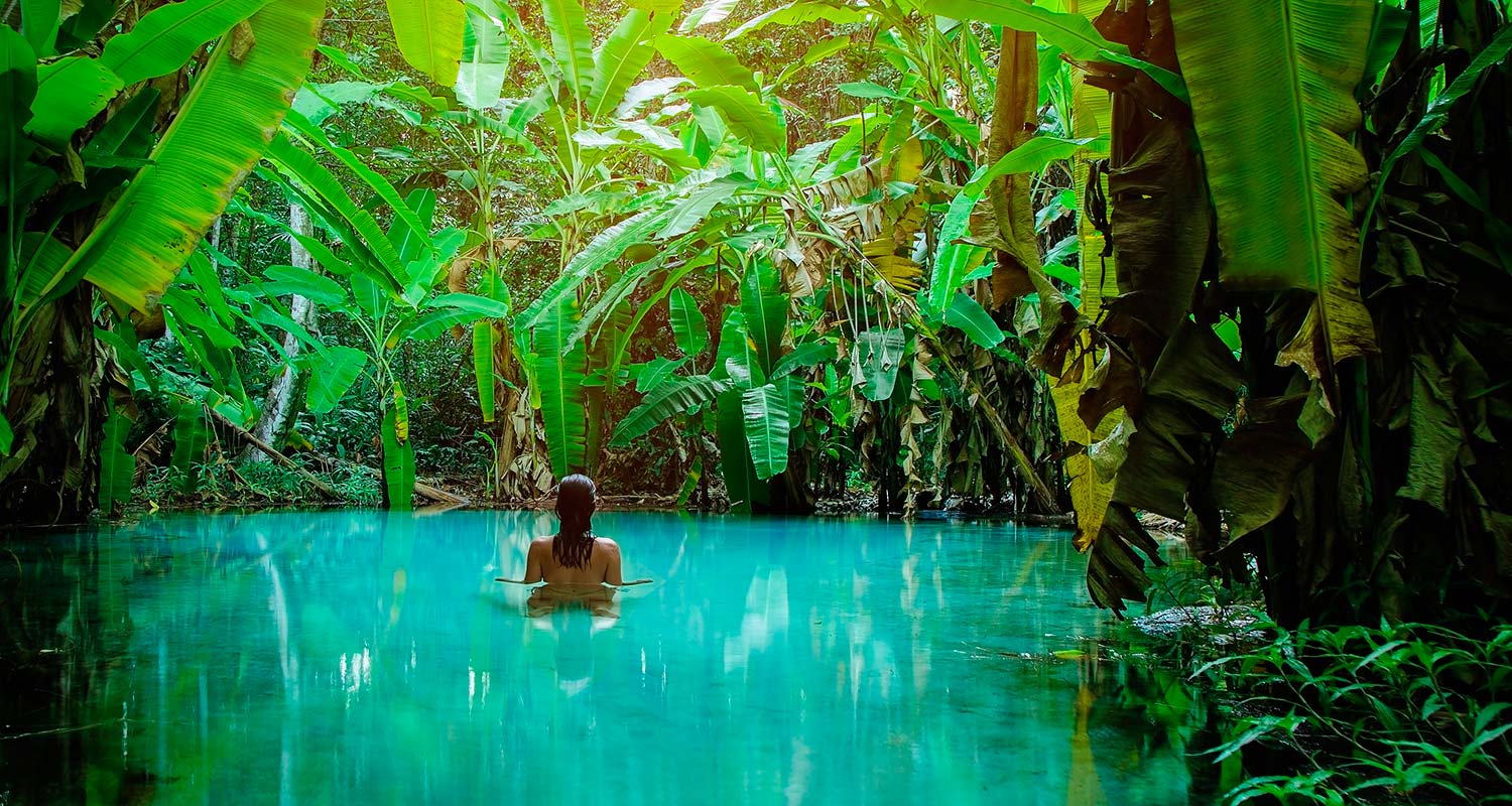 Mulher nadando em uma lagoa de águas azul-turquesa cercada por vegetação exuberante no Jalapão