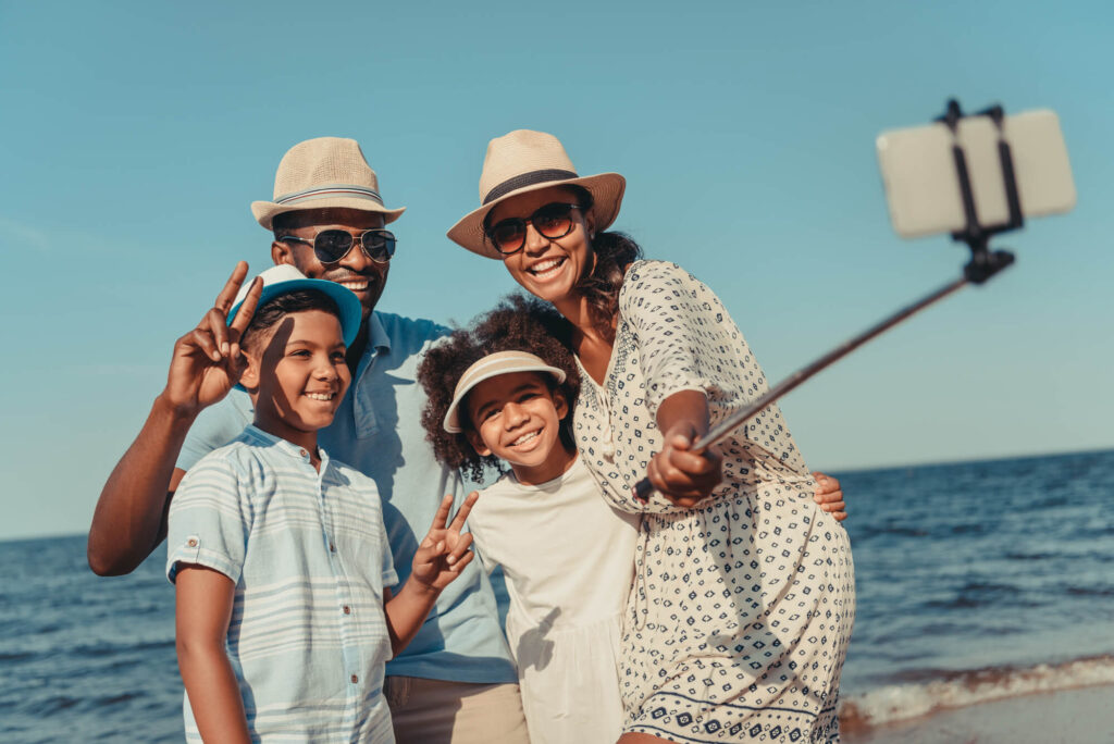 Família multigeracional sorrindo e tirando uma selfie na praia, representando o turismo multigeracional, uma tendência crescente em viagens.