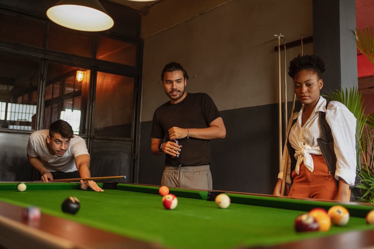 Três jovens brasileiros jogando sinuca, destacando a popularidade e a habilidade necessárias para o esporte no Brasil.