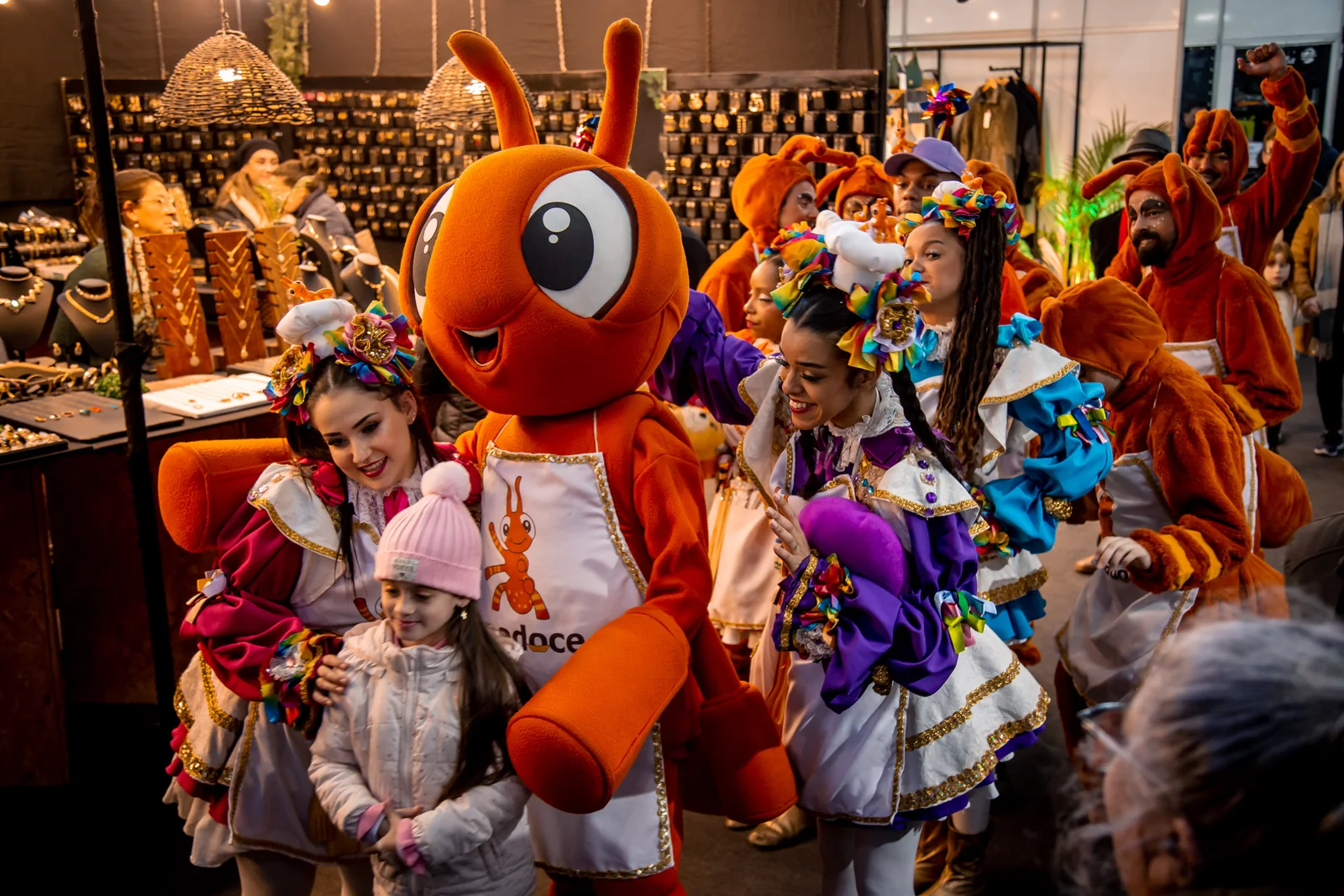 Mascote "Docília" da Fenadoce interage com crianças e visitantes durante o evento em Pelotas, Rio Grande do Sul.