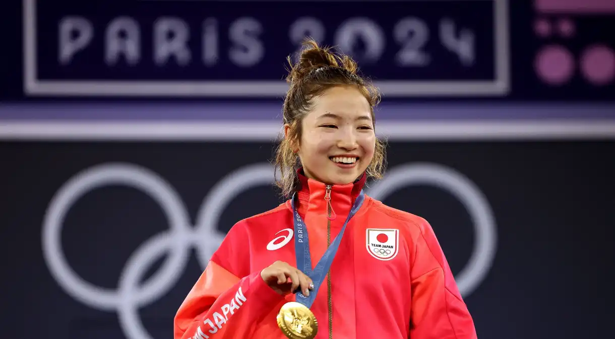 Atleta japonesa sorridente segura sua medalha de ouro nas Olimpíadas de Paris 2024.