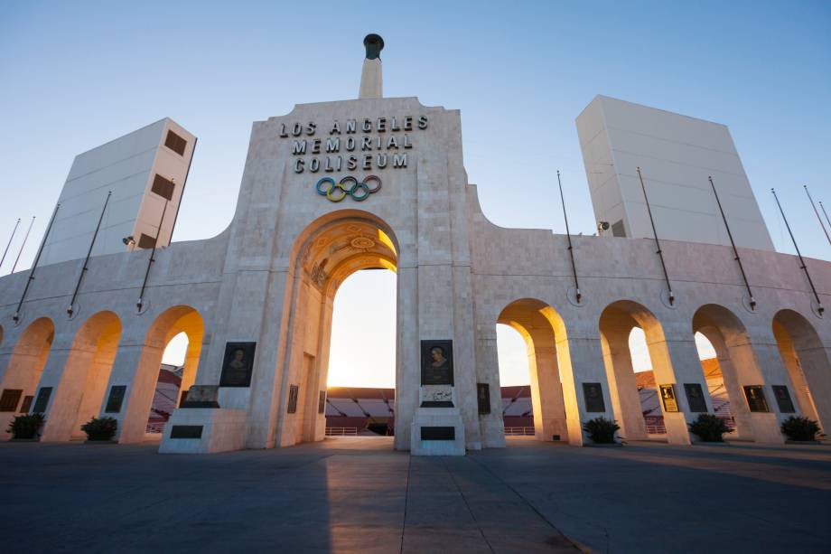 Entrada do Los Angeles Memorial Coliseum ao pôr do sol, com o símbolo olímpico destacado acima do arco.