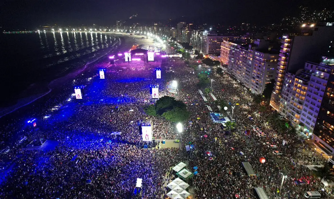 Multidão na Praia de Copacabana durante o show de Madonna no Rio de Janeiro, vista aérea à noite.