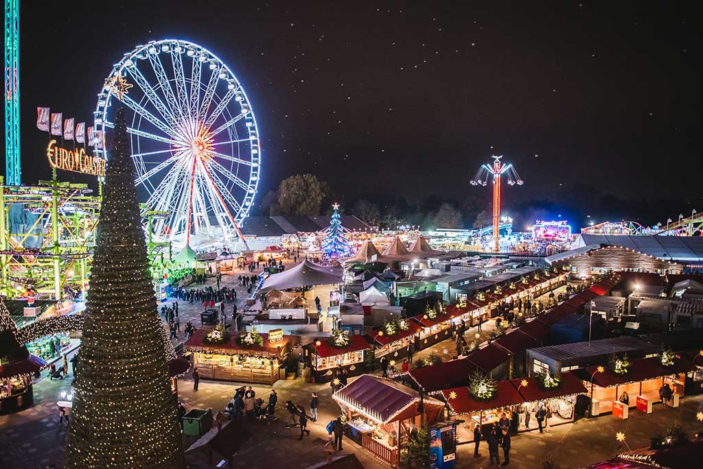 Feira de Natal em Londres iluminada à noite, com uma grande roda-gigante e diversas barracas decoradas.