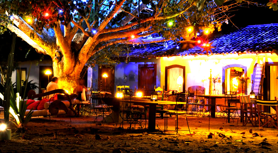 O Quadrado de Trancoso iluminado à noite, com mesas ao ar livre e luzes coloridas nas árvores.