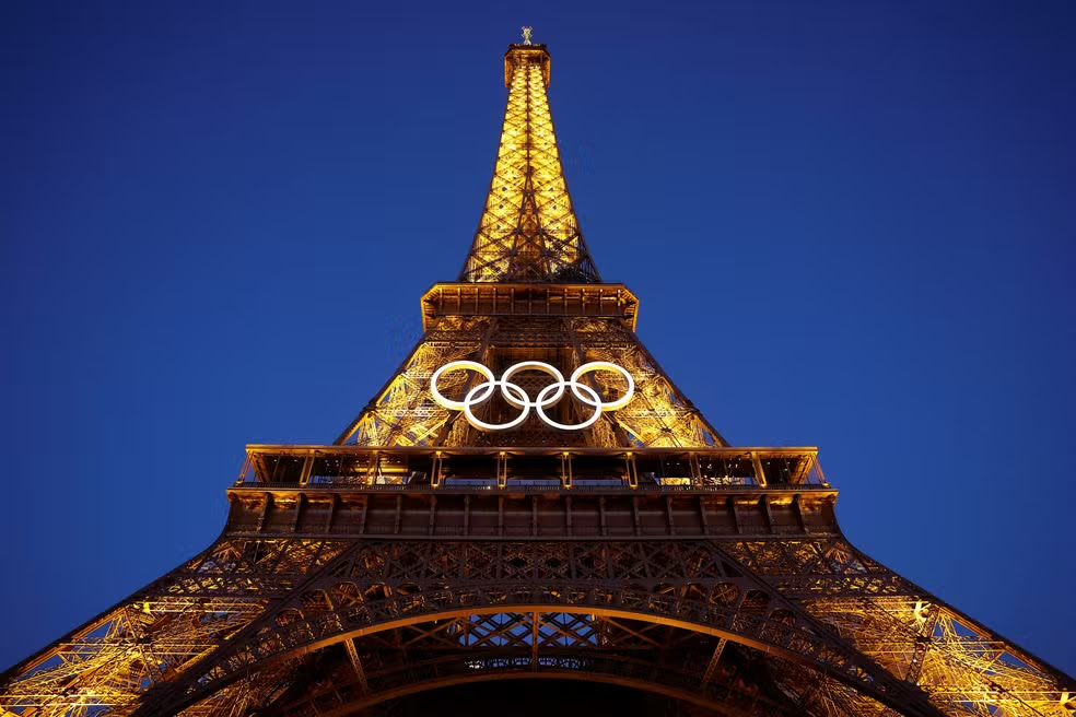 A Torre Eiffel iluminada à noite, exibindo os anéis olímpicos em preparação para as Olimpíadas de Paris 2024