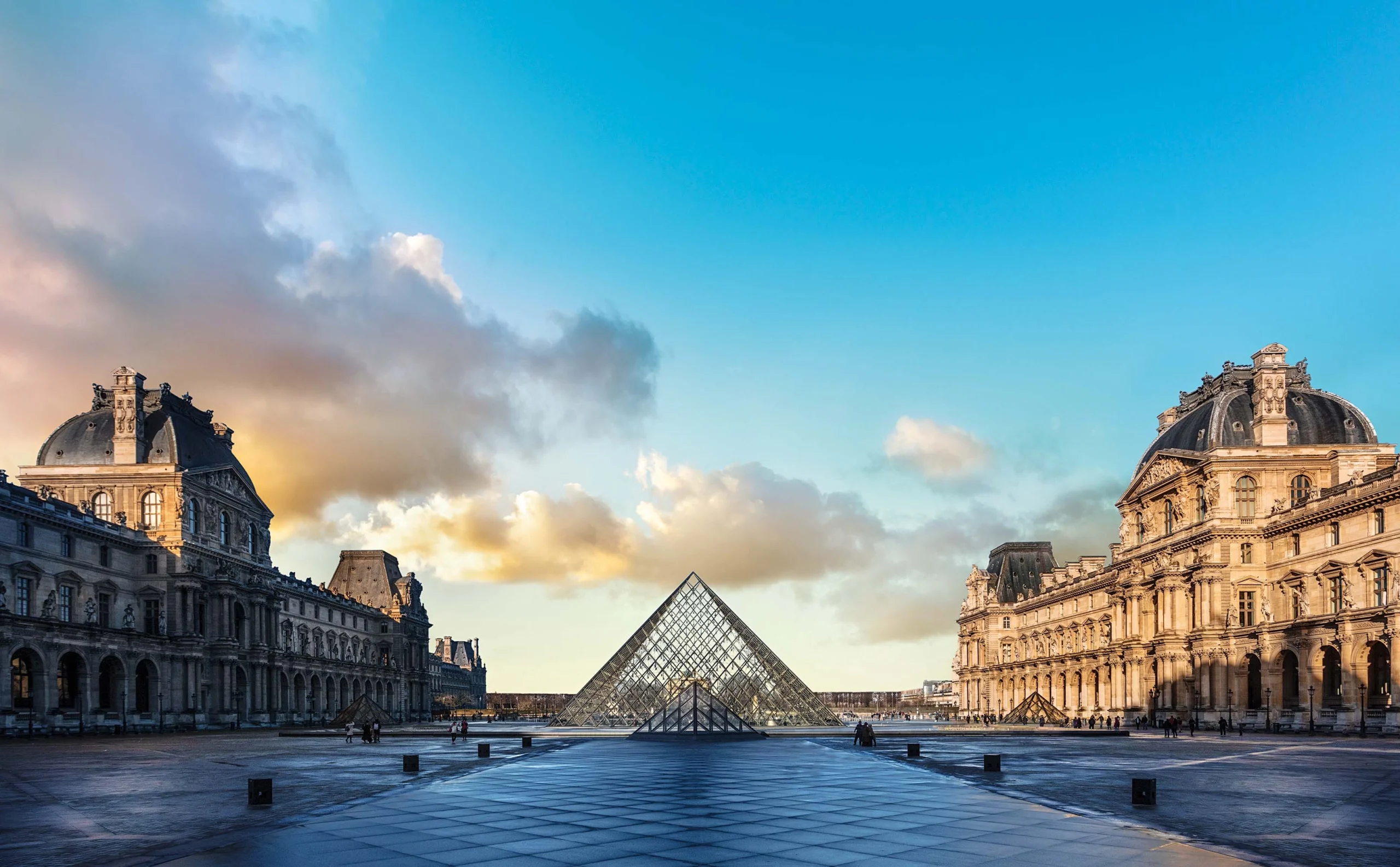 Vista frontal da Pirâmide do Louvre, com a arquitetura clássica do Museu do Louvre ao fundo, em Paris, durante o amanhecer.