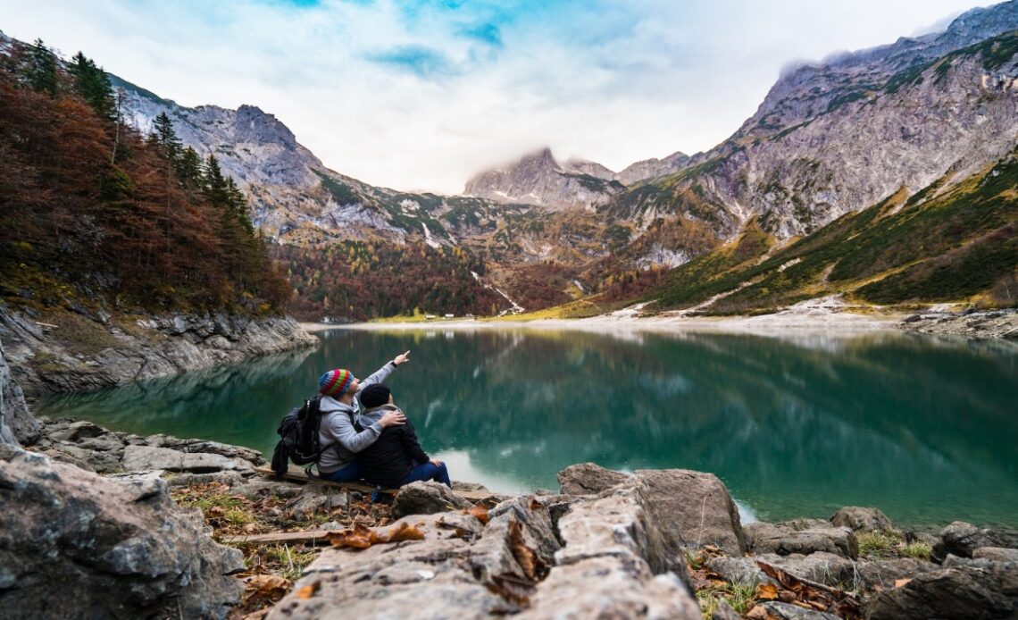 Casal aprecia paisagem montanhosa e lago sereno, simbolizando a personalização e sustentabilidade nas viagens de 2024.