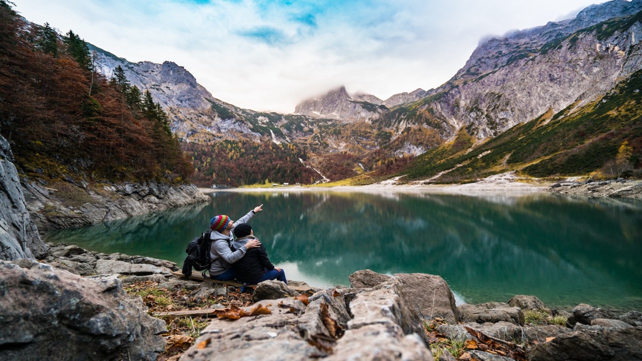 Casal aprecia paisagem montanhosa e lago sereno, simbolizando a personalização e sustentabilidade nas viagens de 2024.