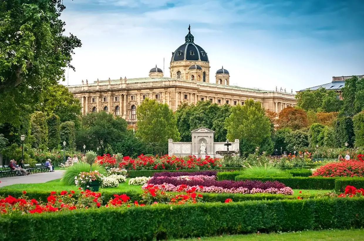 Jardins floridos em Viena com um grandioso edifício histórico ao fundo, em um dia claro.