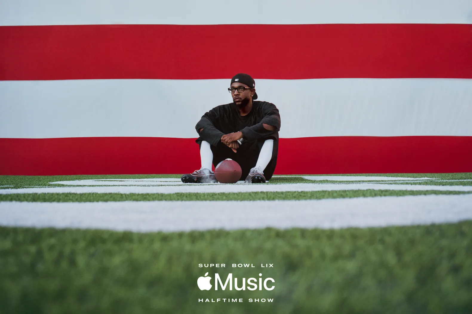 Kendrick Lamar sentado em campo de futebol americano com bola ao lado, promovendo seu show no intervalo do Super Bowl LIX, um evento da NFL, ligado ao turismo em Nova Orleans.