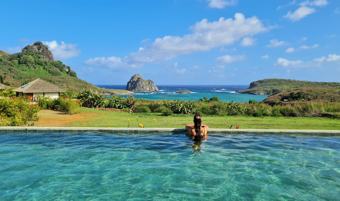 Mulher relaxando em uma piscina com vista para os morros e o mar em Fernando de Noronha, um dos paraísos nacionais do Brasil.