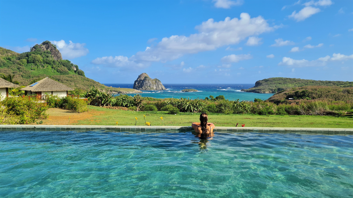 Mulher relaxando em uma piscina com vista para os morros e o mar em Fernando de Noronha, um dos paraísos nacionais do Brasil.