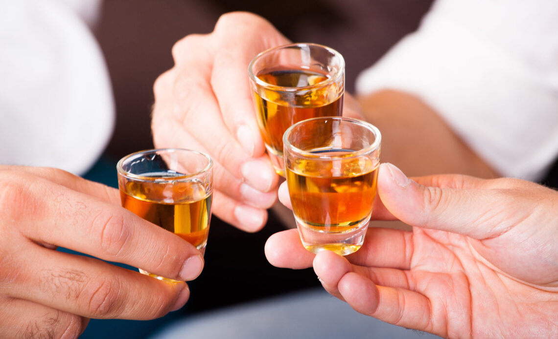 Três pessoas brindando com doses de cachaça em copos de vidro.