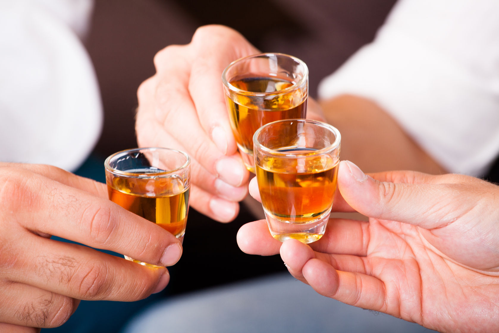 Três pessoas brindando com doses de cachaça em copos de vidro.