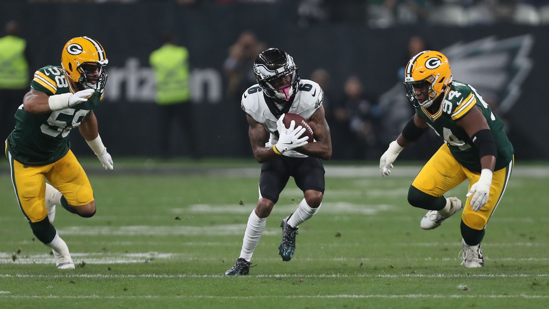 Jogador do Philadelphia Eagles avança com a bola sendo perseguido por dois jogadores do Green Bay Packers em uma partida da NFL, conectando futebol americano ao turismo.