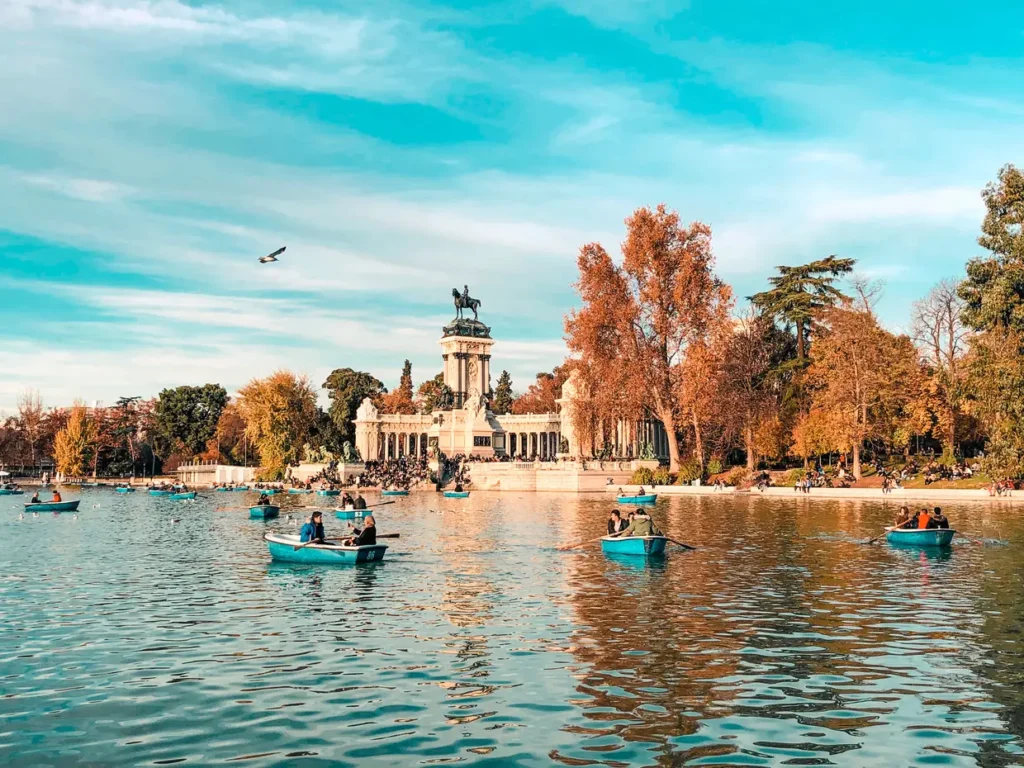 Barcos a remo no lago do Parque Retiro em Madrid, com o Monumento a Afonso XII ao fundo em um dia ensolarado de outono.