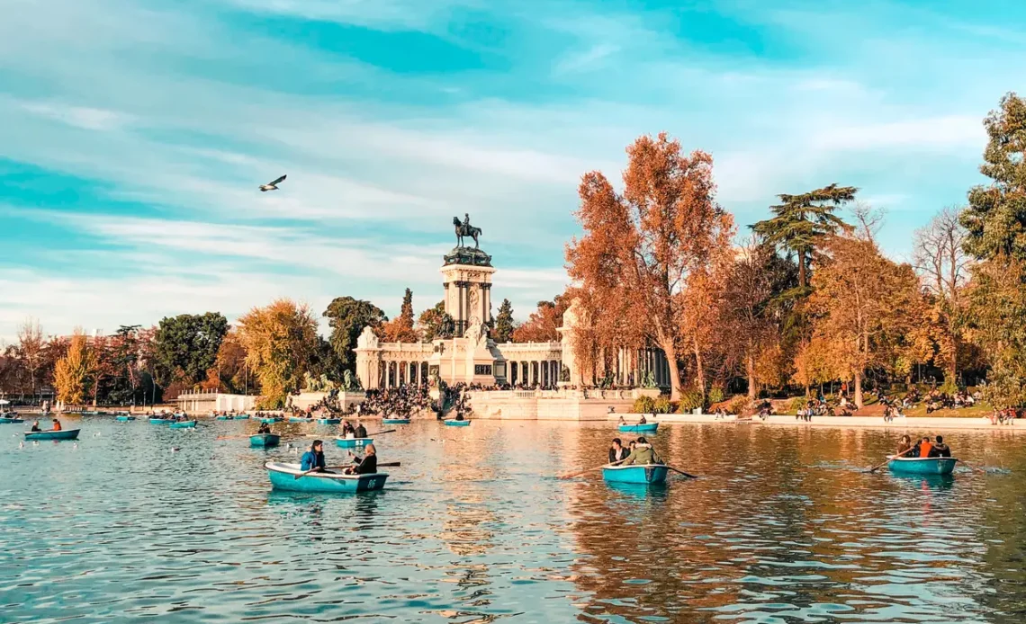 Barcos a remo no lago do Parque Retiro em Madrid, com o Monumento a Afonso XII ao fundo em um dia ensolarado de outono.