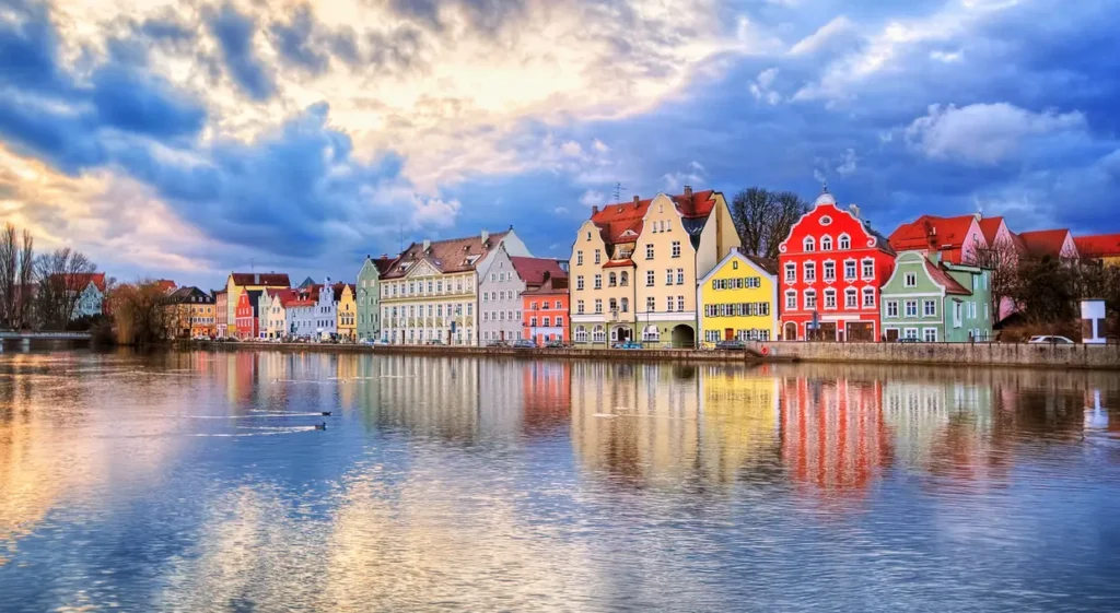 Casas coloridas refletidas no rio em uma cidade histórica da Europa, sob um céu nublado ao pôr do sol. Eurotrip.