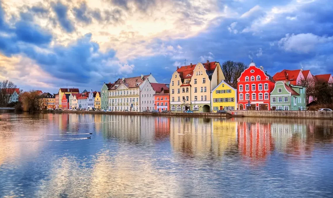 Casas coloridas refletidas no rio em uma cidade histórica da Europa, sob um céu nublado ao pôr do sol. Eurotrip.