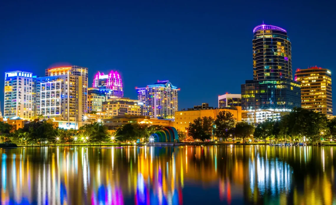 Vista noturna do centro de Orlando, com prédios iluminados refletindo no lago.