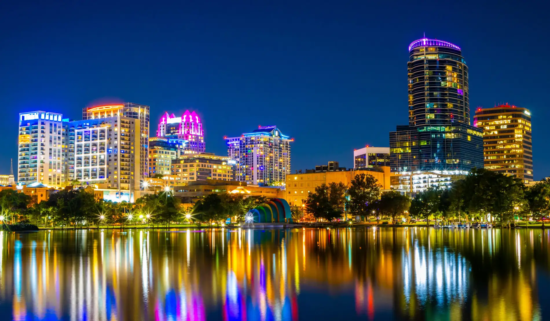 Vista noturna do centro de Orlando, com prédios iluminados refletindo no lago.