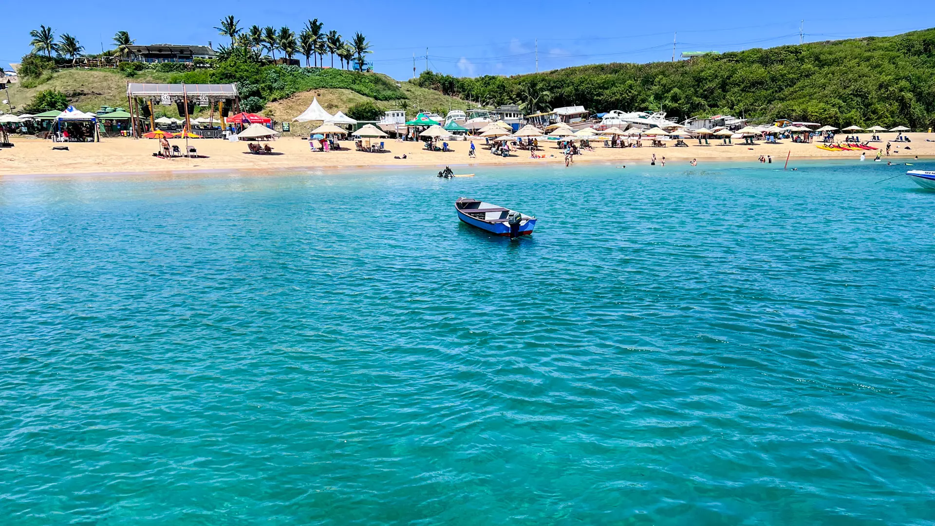 Vista da Praia do Porto em Fernando de Noronha, com barco flutuando nas águas cristalinas.