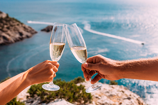 Brinde romântico com taças de champagne em frente a um cenário costeiro deslumbrante.