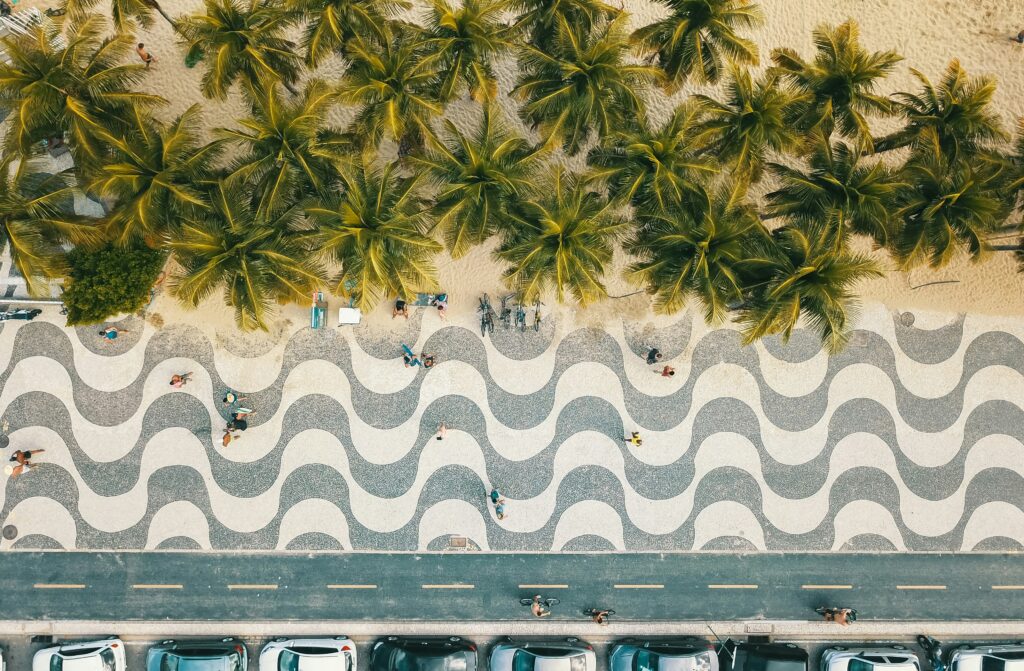 Vista aérea do calçadão de Copacabana no Rio de Janeiro, onde Eduardo Paes anunciou os shows do Réveillon 2025, mostrando a icônica calçada ondulada cercada por palmeiras e a praia ao fundo.