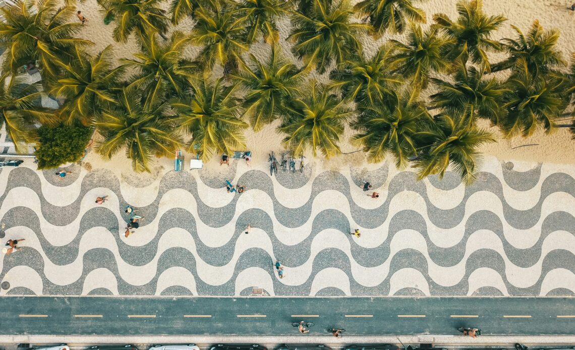 Vista aérea do calçadão de Copacabana no Rio de Janeiro, onde Eduardo Paes anunciou os shows do Réveillon 2025, mostrando a icônica calçada ondulada cercada por palmeiras e a praia ao fundo.