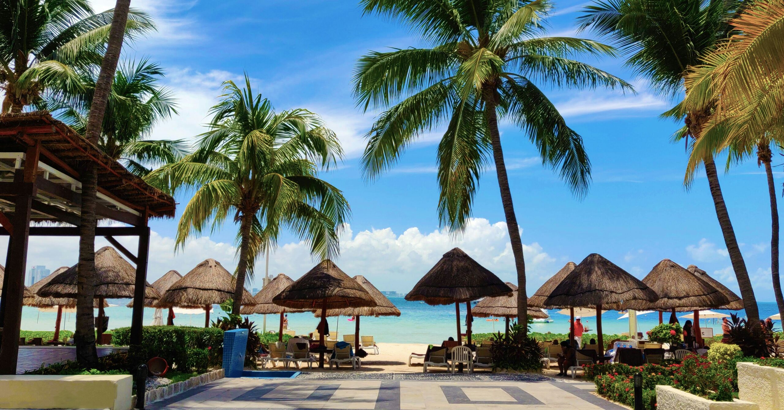 Vista de praia tropical com palmeiras, guarda-sóis de palha e espreguiçadeiras em um resort all-inclusive em Cancun.