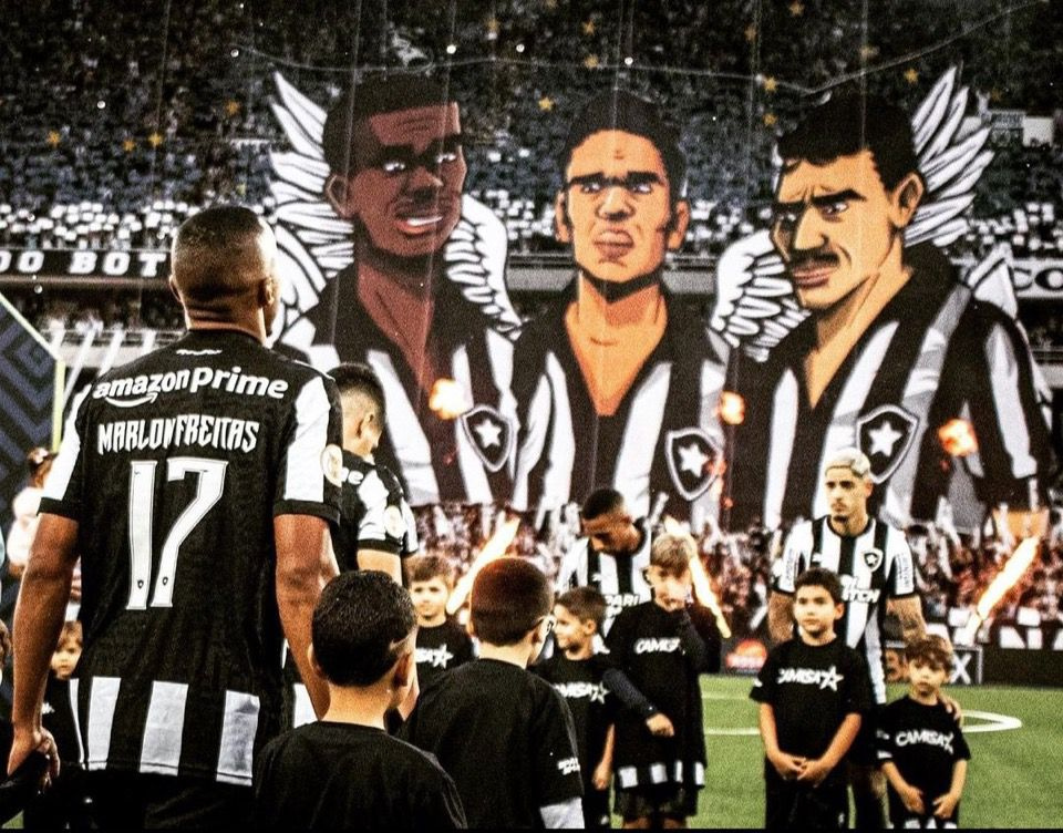 Jogadores do Botafogo entram em campo sob um mosaico com ídolos históricos, marcando um momento decisivo no Brasileirão e na Libertadores.