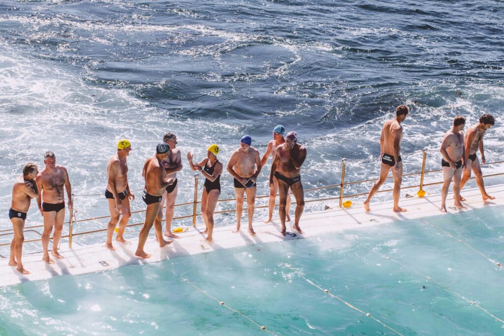 Grupo de idosos na beira de uma piscina de frente para o mar, em um dia ensolarado.