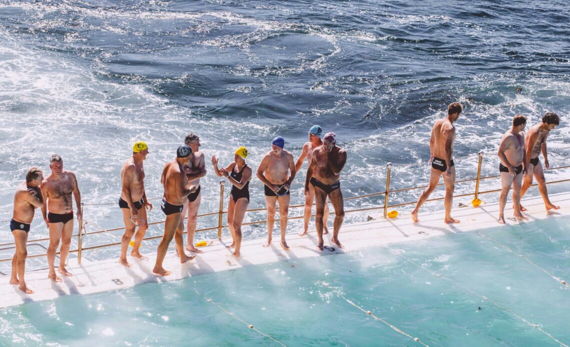 Grupo de idosos na beira de uma piscina de frente para o mar, em um dia ensolarado.