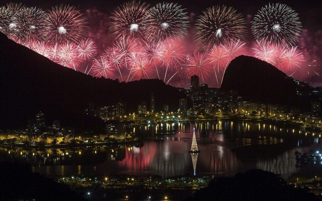 Show de fogos no Réveillon do Rio de Janeiro refletido na Lagoa Rodrigo de Freitas, com a árvore de Natal iluminada.