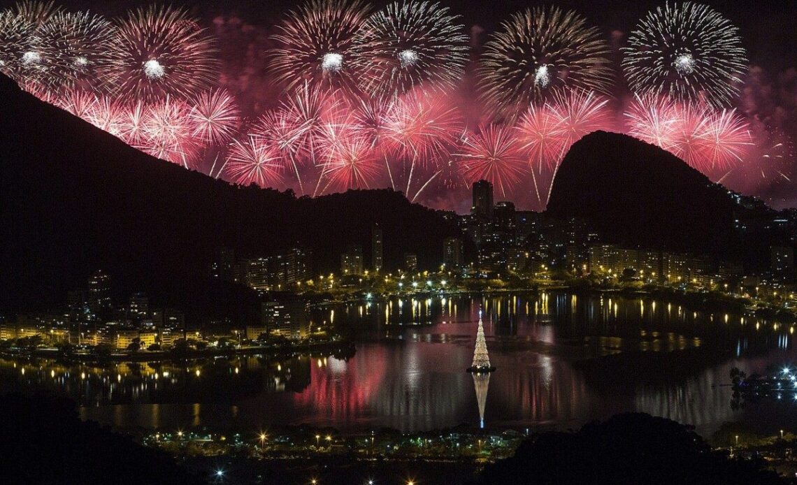 Show de fogos no Réveillon do Rio de Janeiro refletido na Lagoa Rodrigo de Freitas, com a árvore de Natal iluminada.