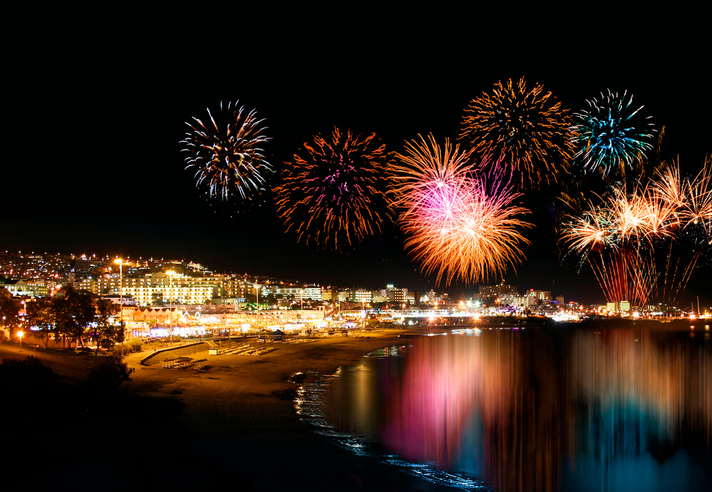 Queima de fogos em Ilhabela, São Paulo, iluminando a noite sobre a orla e as águas calmas, cenário ideal para o Réveillon 2025.