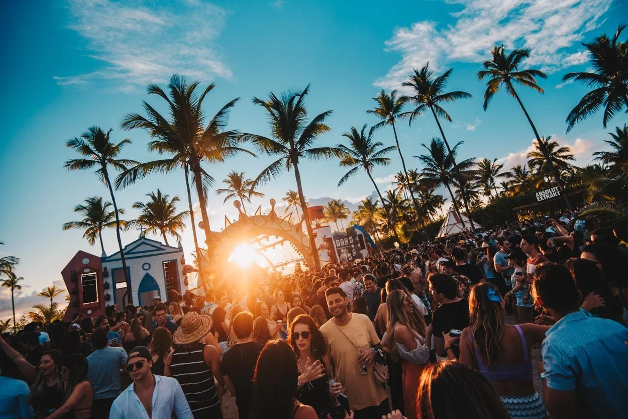 Festa ao pôr do sol em Maragogi, Alagoas, com palmeiras, música e pessoas celebrando o Réveillon 2025.