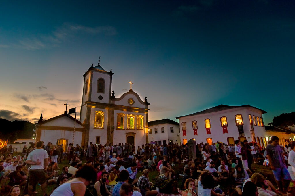 Igreja iluminada ao entardecer em Paraty, Rio de Janeiro, cercada por moradores e turistas, cenário acolhedor para o Réveillon 2025.