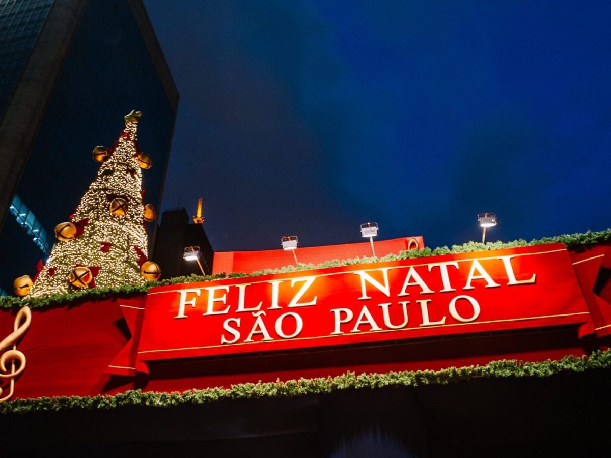 Decoração de Natal em São Paulo com uma grande árvore iluminada e um painel vermelho escrito 'Feliz Natal São Paulo' ao fundo, destacando o clima natalino na cidade.