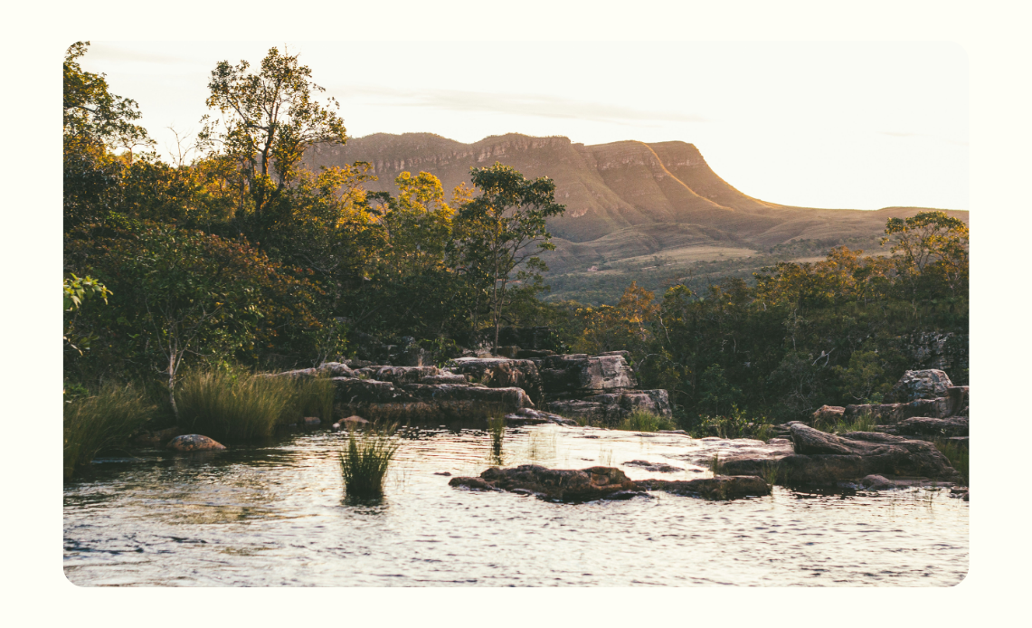 Paisagem do Parque Nacional da Chapada dos Veadeiros, em Goiás, com vegetação do cerrado, pedras e uma formação montanhosa ao fundo iluminada pela luz do pôr do sol.